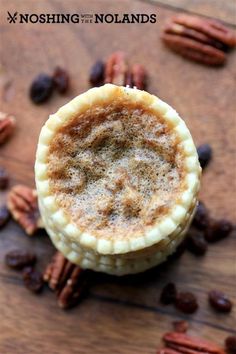 two pecan pies sitting on top of a wooden table with nuts around them