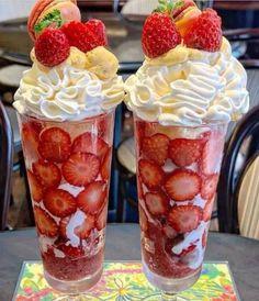 two cups with strawberries and whipped cream on them sitting on a table next to each other