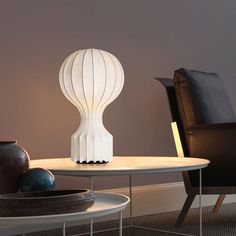 a white lamp sitting on top of a table next to a black chair and vase