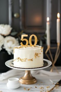 a white cake with gold numbers on it sitting on a table next to some candles