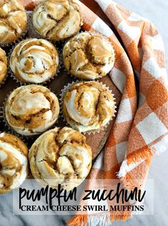 pumpkin muffins with cream cheese swirl topping on a wooden plate next to an orange and white checkered towel