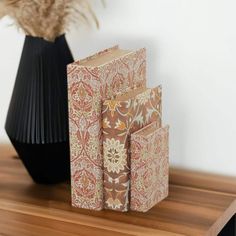 three books sitting on top of a wooden table next to a vase with dried flowers