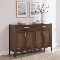 a sideboard with two pictures on the wall above it and a vase filled with flowers