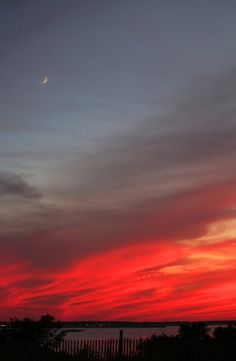 the sky is red and blue as the sun sets in the distance with a few clouds