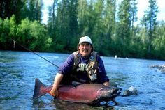 a man sitting in the middle of a river with a large fish on it's back