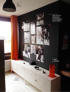 a living room with black walls and pictures on the wall, along with orange curtains