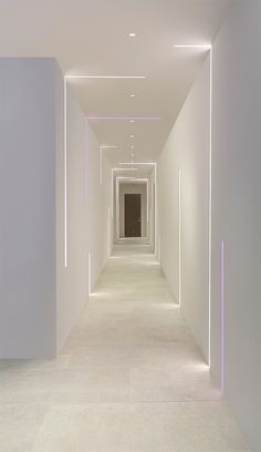 an empty hallway with white walls and purple light at the end is lit by neon lights