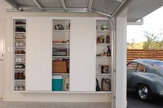 a car is parked in the garage with its doors open and shelves full of items