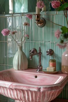 a pink sink in a bathroom with flowers on the counter and green tile behind it