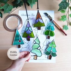 a hand holding a pair of scissors next to stained glass christmas trees