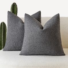 two gray pillows sitting on top of a white couch next to a green cactus plant