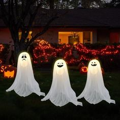 three ghost statues in front of a house decorated with lights and pumpkins for halloween