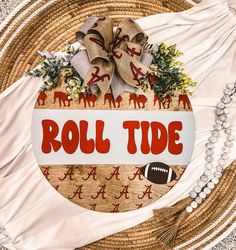 a sign that says roll tide on it with a football and wreath next to it