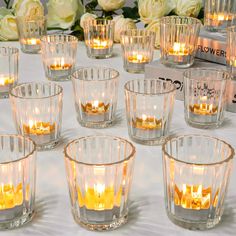 many clear glass cups with candles in them on a white tablecloth and some flowers