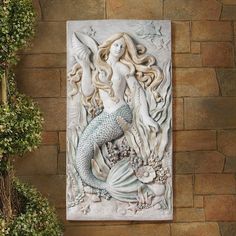 a mermaid statue sitting on top of a brick wall next to a potted plant