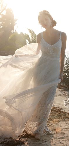 a woman is walking on the beach with her dress blowing in the wind