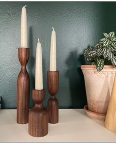 three wooden candlesticks sitting on top of a table next to a potted plant