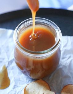 an apple cider being poured into a glass jar filled with caramel sauce and sliced apples