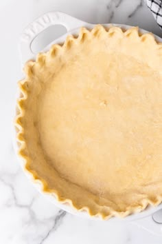 an uncooked pie crust in a white dish on a marble countertop next to a black and white checkered napkin