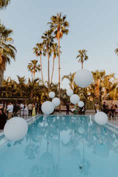 white balloons floating in the air over a pool surrounded by palm trees and people sitting at tables