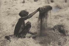 a person kneeling down in the grass with their arm extended out to grab something from the ground