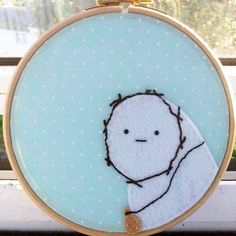 the embroidery is hanging on the window sill and there is a small white face with brown hair