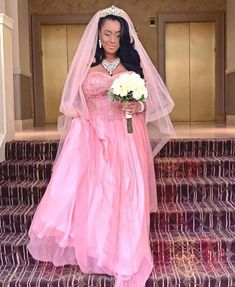 a woman in a pink wedding gown standing on some steps with flowers and a bouquet