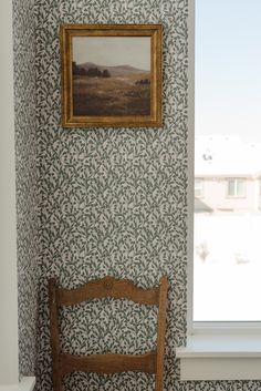 a wooden chair sitting in front of a window next to a painting on the wall