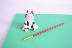 a toy cow sitting next to a paintbrush on a green surface with a red pencil