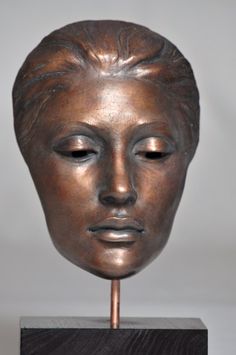 a bronze sculpture of a woman's face on a wooden stand with eyes closed