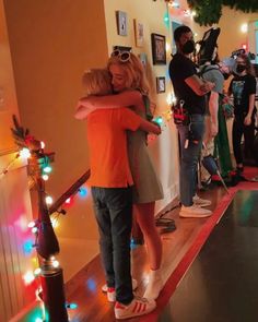 two people hugging each other in front of a group of people with lights on the wall