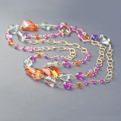 Long, gold filled, wire wrapped necklace featuring beautiful sapphires and spinel.  This 36 inch long necklace is crafted with unique, free form, step cut  nuggets of orange sapphire  ovals of pale green, micro faceted  amethyst, smooth polished bright pink sapphire nuggets and bright pink roundels of spinel. These gems are wrapped with gold filled wire into colorful sections separated by delicate gold filled, textured  chain. This necklace looks and feels luxurious it is  perfect for a boho look or layered, showing off both beautiful array of gems and delicate chain.  Beautiful!  Only one available, you will receive the necklace shown. Green amethyst 9x11mm  Orange sapphire nuggets to 13x17mm Multicolor Gemstone Long Crystal Necklace, Pink Beaded Amethyst Necklace, Multicolor Amethyst Multi-stone Necklaces, Luxury Amethyst Multi-stone Necklaces, Hand-strung Pink Rose Quartz Necklace, Orange Sapphire, Bohemian Necklace, Wire Wrapped Necklace, Green Amethyst