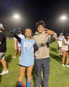 a man and woman standing on top of a soccer field at night with their arms around each other