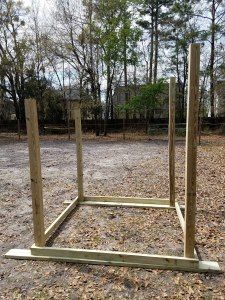 a wooden structure sitting in the middle of a field with leaves on the ground and trees behind it