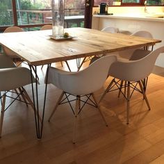 a wooden table surrounded by white chairs in a room with wood floors and large windows