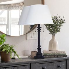 a lamp is sitting on top of a dresser next to a mirror and potted plants