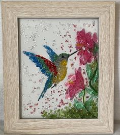 a hummingbird sitting on top of a flower next to a pink flower in a wooden frame