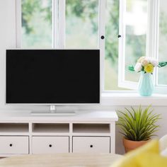 a flat screen tv sitting on top of a white entertainment center next to a window