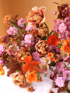 a bunch of flowers that are on a white table cloth and some brown, pink, orange and yellow flowers