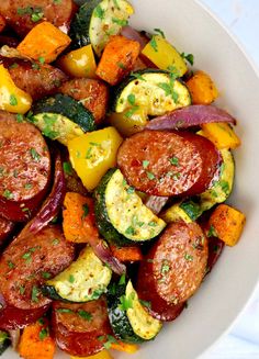 a white bowl filled with sausage and veggies on top of a marble table