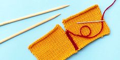 two knitting needles and an orange piece of cloth next to some knitting needles on a blue surface