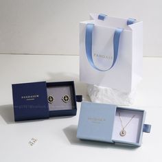 an open box with two necklaces in it sitting next to a pair of earrings