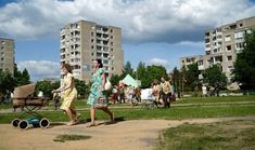 two women walking down a dirt road in front of apartment buildings and a baby stroller