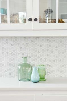 two green vases sitting on top of a white counter next to a glass cabinet