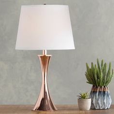 a table lamp sitting on top of a wooden table next to a potted plant