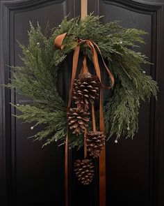 a wreath with pine cones and ribbons hanging on the front door to decorate it for christmas