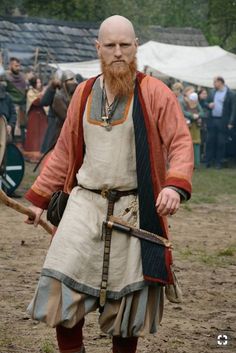 a bearded man dressed in medieval clothing holding a stick