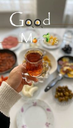 a person is holding a glass of tea in front of a table full of food