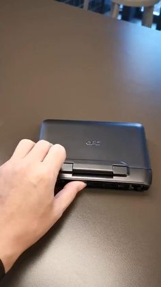 a person is using their hand to open the back cover of a laptop on a table