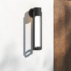 a wall mounted light on the side of a white building next to a wooden door